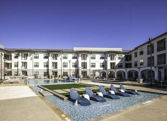 a pool with blue chairs in front of an apartment building