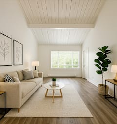 A living room with a beige couch, a white coffee table, and a large window.