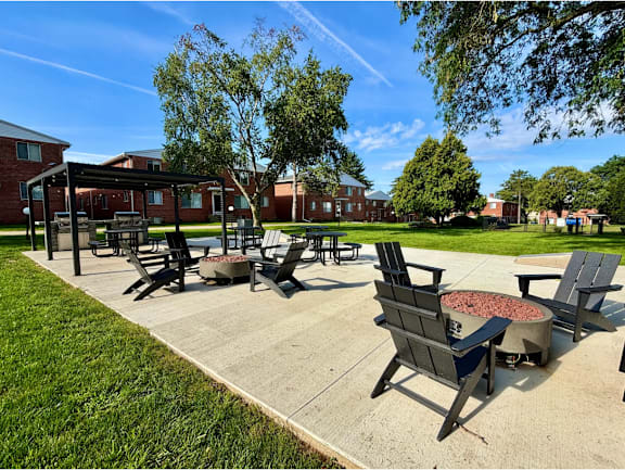 A sunny day at a park with a fire pit and chairs.