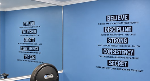 A gym room with a row of exercise machines and a wall with inspirational words.