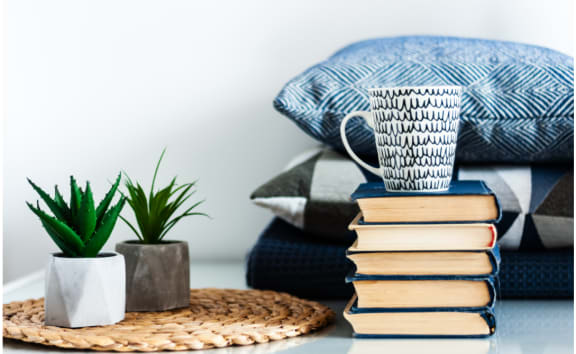 a pile of books on a table with plants and pillows