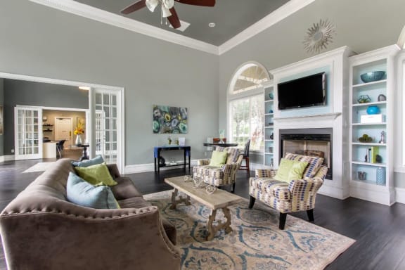 Clubhouse Seating Area with Large Windows on either side of Fireplace with TV and Shelves Surrounding Fireplace Multi Colored Accent Chairs Grey Couch and Clubhouse Foyer in the Background