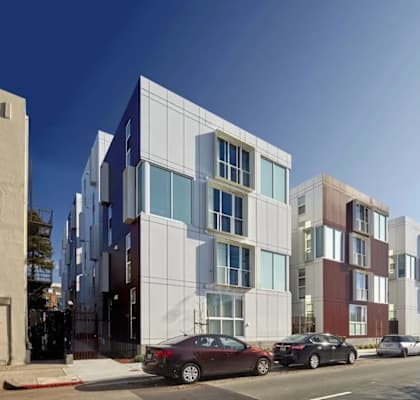 A row of modern apartment buildings with cars parked in front.
