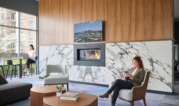 A woman is sitting in a chair in a room with a fireplace and a painting on the wall.