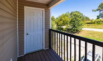 a white door opens to a balcony with a blue sky and trees in the background