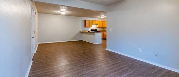 an empty living room with a ceiling fan and a kitchen in the background