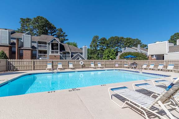A swimming pool surrounded by lounge chairs and buildings in the background.