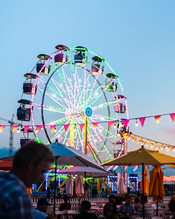 A large Ferris wheel is lit up with colorful lights at dusk.