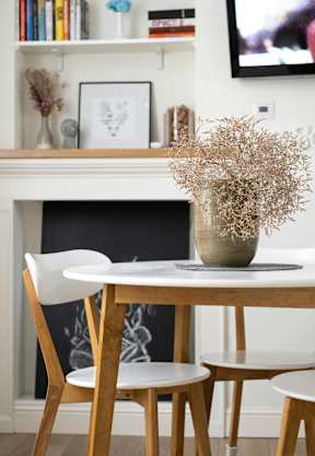 A white table with two chairs and a vase of dried flowers placed on top.