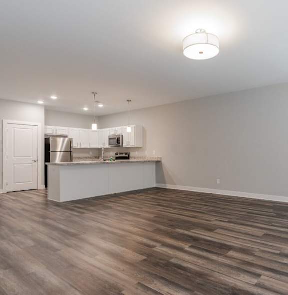 A room with wooden flooring and a kitchenette in the background.
