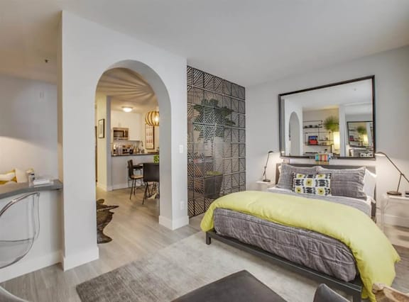 A bedroom with a bed, a desk, and a mirror.