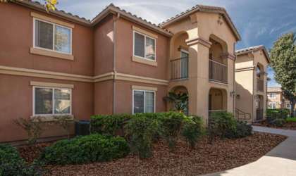A building with a red stucco exterior and a landscaped front yard.
