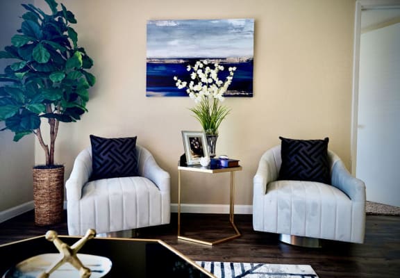 a living room with two white chairs and a table with a vase of flowers