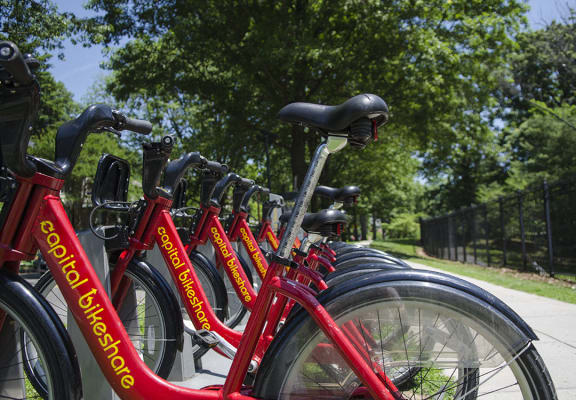 A row of red Capital BikeShare bicycles are parked on a sidewalk. at Park Crest Apartments, District of Columbia 20007