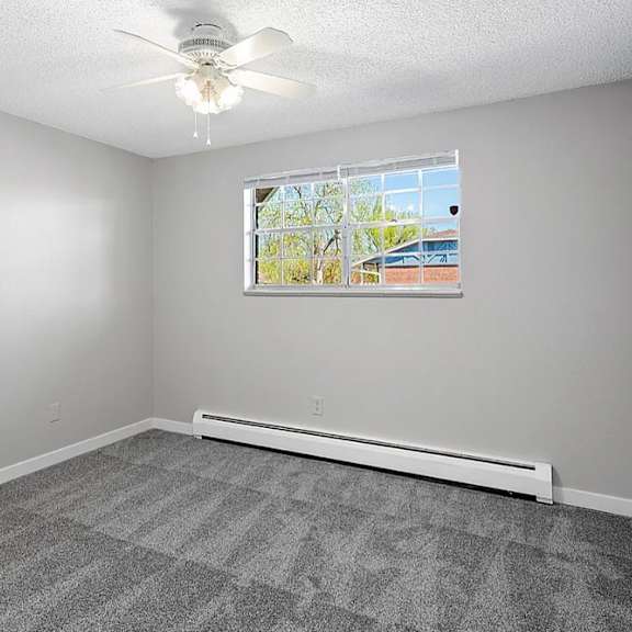 A room with a ceiling fan and a window with a view of a building outside.
