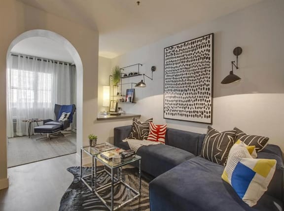 A living room with a blue couch and a glass table.