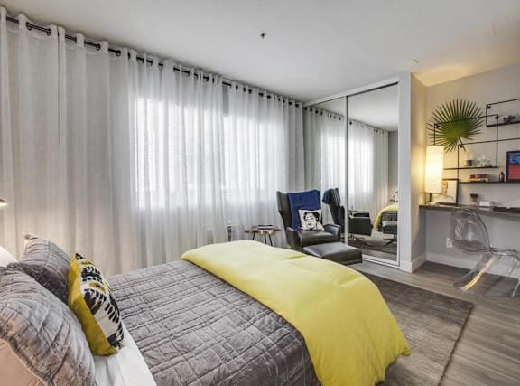 A bedroom with a bed covered in a yellow comforter and a grey headboard.