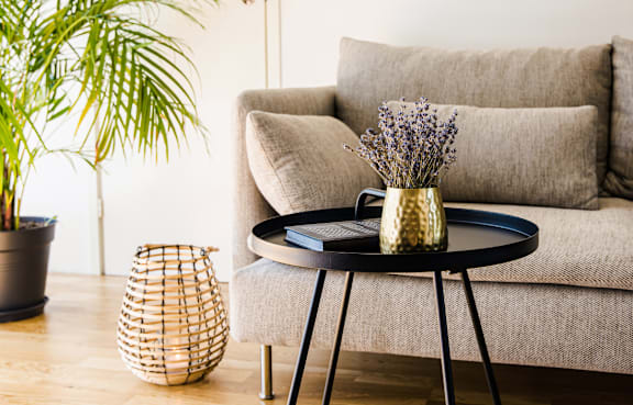 A living room with a grey couch, a round table with a vase of flowers on it, and a woven basket on the floor.