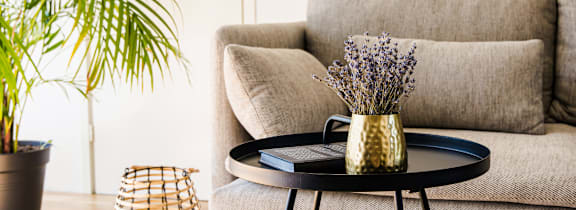 A living room with a grey couch, a round table with a vase of flowers on it, and a woven basket on the floor.