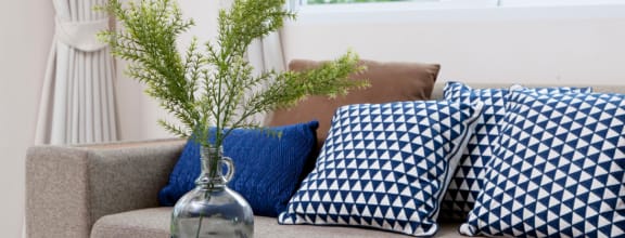 a couch with blue and white pillows and a glass vase with some flowers