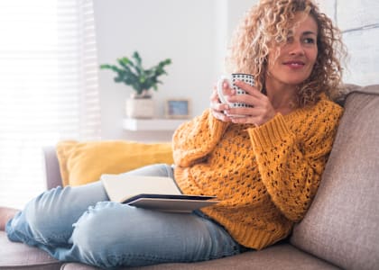 a woman sitting on a couch with a drink and a book