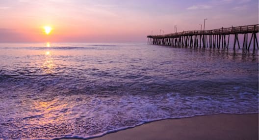 A sunset view of a beach with a pier in the background.