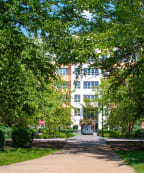 a large brick building with a driveway in the foreground and a parking lot in the background