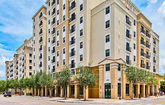 A large, beige hotel with a row of trees in front.