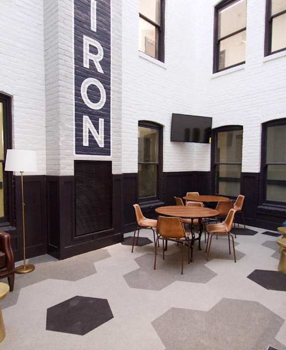 A room with a brown leather couch, a wooden table and chairs, and a black and white checkered floor.
