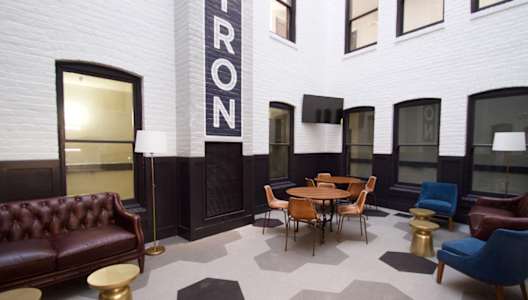 A room with a brown leather couch, a wooden table and chairs, and a black and white checkered floor.