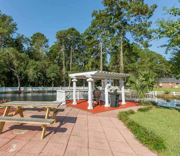A pavilion with picnic tables is surrounded by trees and a body of water.
