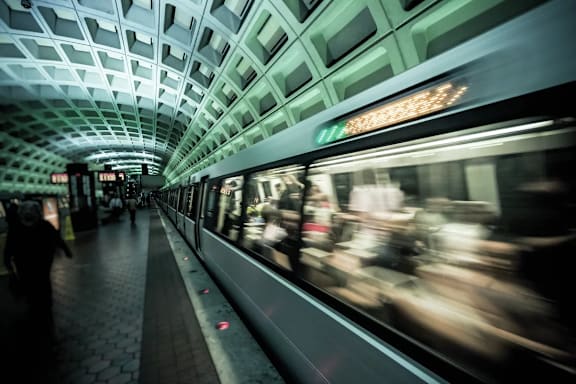 A subway train is passing through a subway station with people walking on the platform.