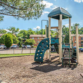 A playground with a green slide, a wooden swing set, and a green bench.