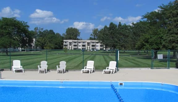 A pool with chairs around it and a building in the background.