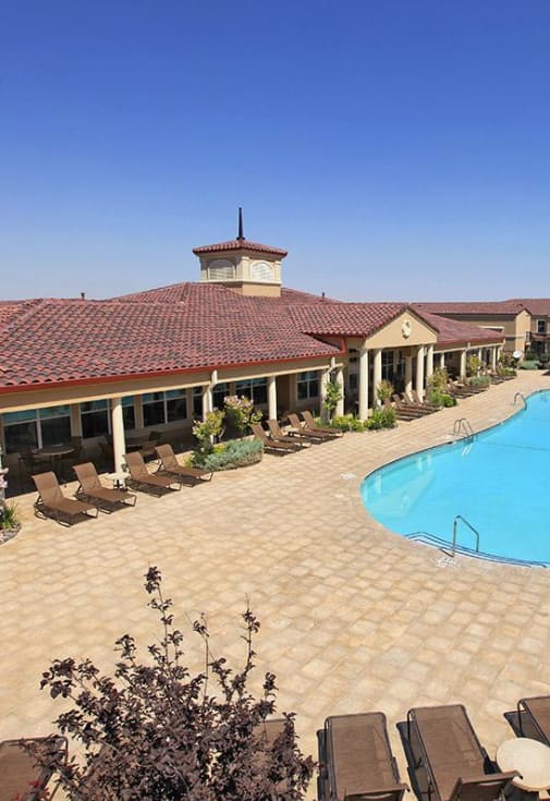 A large outdoor swimming pool surrounded by a tiled patio and lounge chairs.