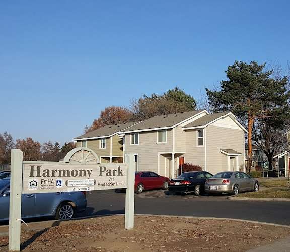 A sign for Harmony Park is in front of a building with cars parked in front.