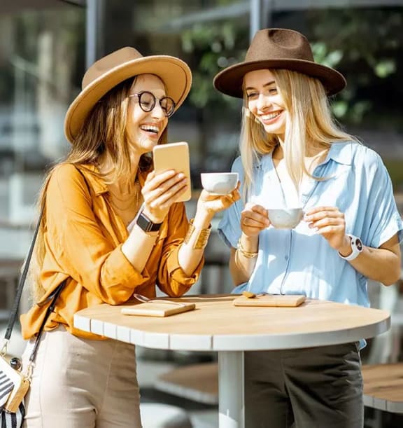 two women sitting at a table drinking coffee and looking at a cell phone