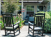 Thumbnail 4 of 5 - Two rocking chairs are on a concrete patio in front of a house.