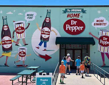 A mural of Dr Pepper bottles and a sign that says "More Exhibits!" are on the side of a building.
