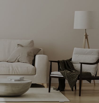 A white couch with a bowl on the floor and a chair with a blanket on it.