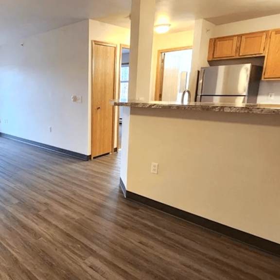 A room with wooden flooring and a kitchen area with a microwave.