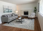 Thumbnail 2 of 8 - A living room with a grey couch, a coffee table, a lamp, a fireplace, and a chair.