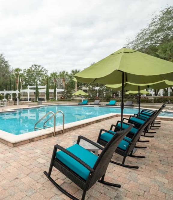 a swimming pool with lounge chairs and umbrellas in front of a brick building