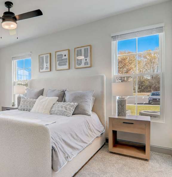 A bedroom with a large bed, a ceiling fan, and pictures on the wall.