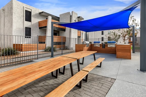 A blue shade sail over a wooden picnic table.