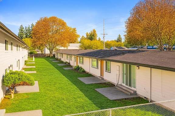 A row of houses with green lawns and trees in the background.