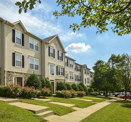 A row of townhouses with green lawns and trees in the background.
