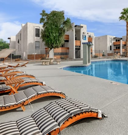 A pool area with sun loungers and a building in the background.
