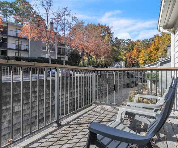 A balcony with a black chair and table is surrounded by a metal railing.