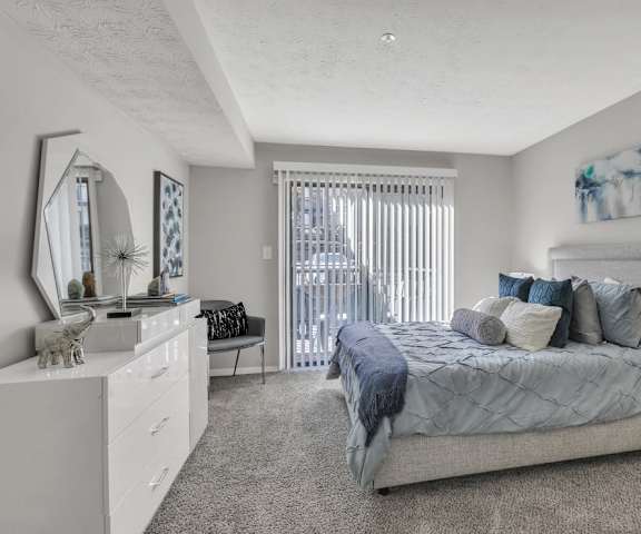 A bedroom with a large bed, a vanity with a mirror, and a window with blinds.